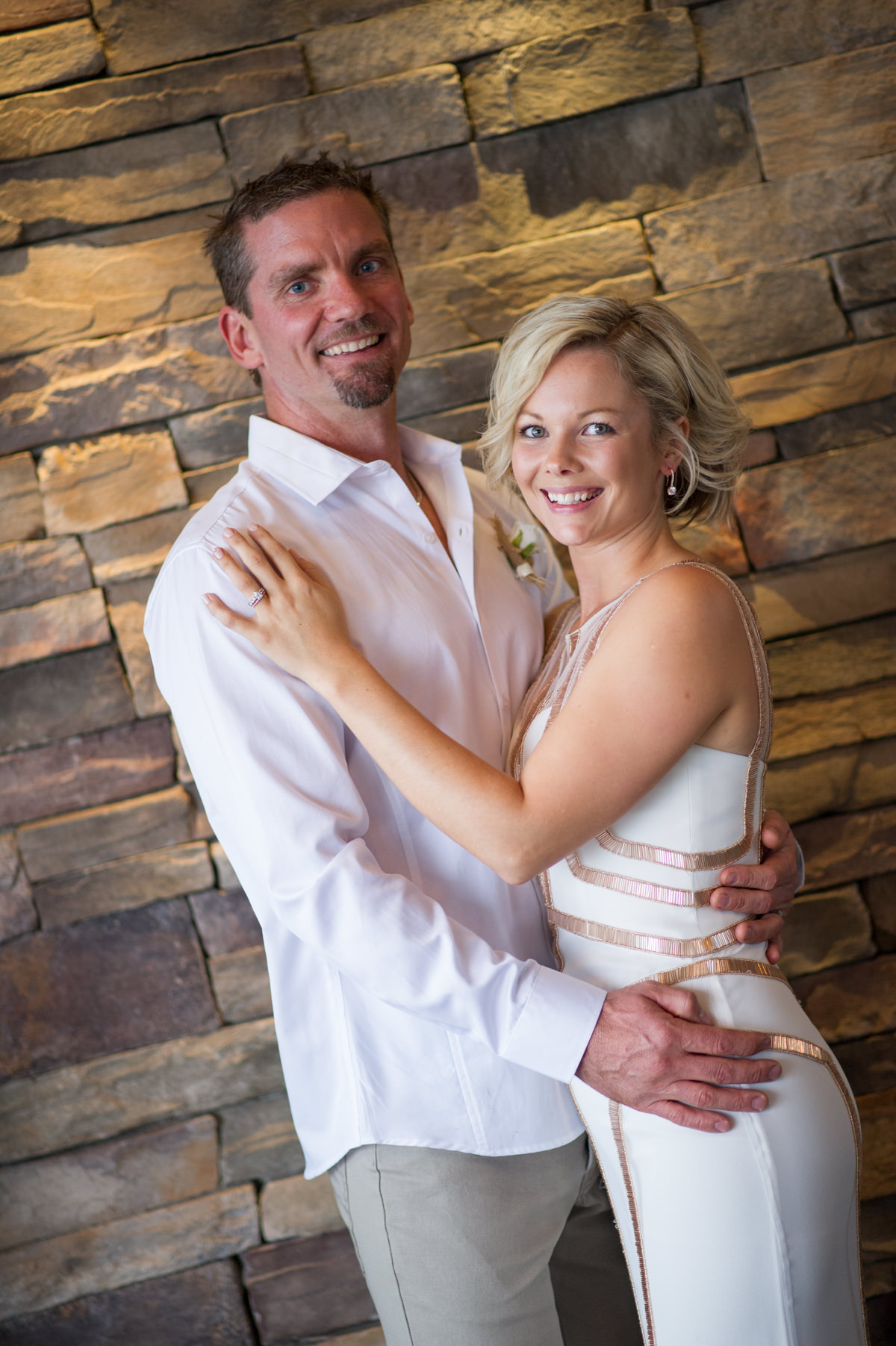 Bride and groom standing against brick wall at The Breakwater