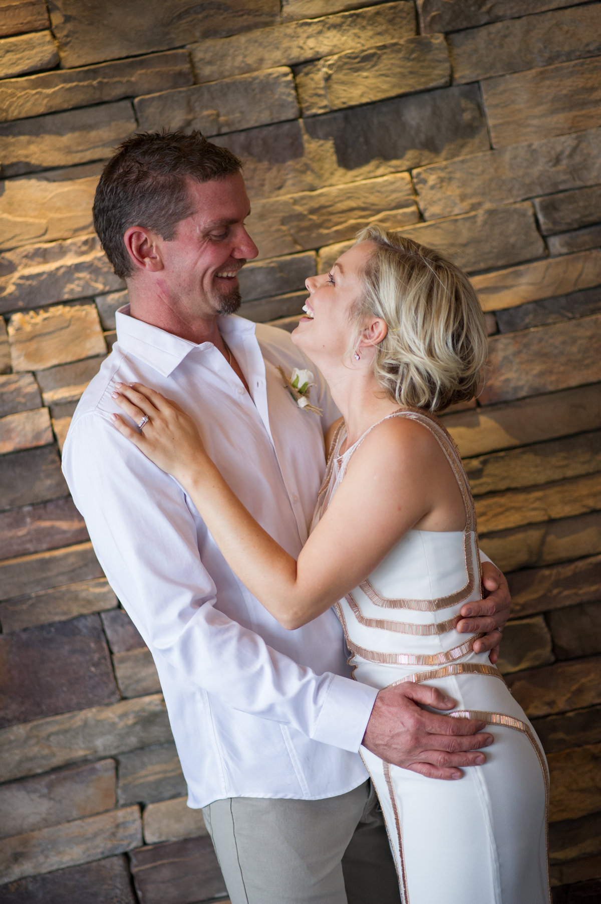 Bride and groom standing against brick wall at The Breakwater laughing