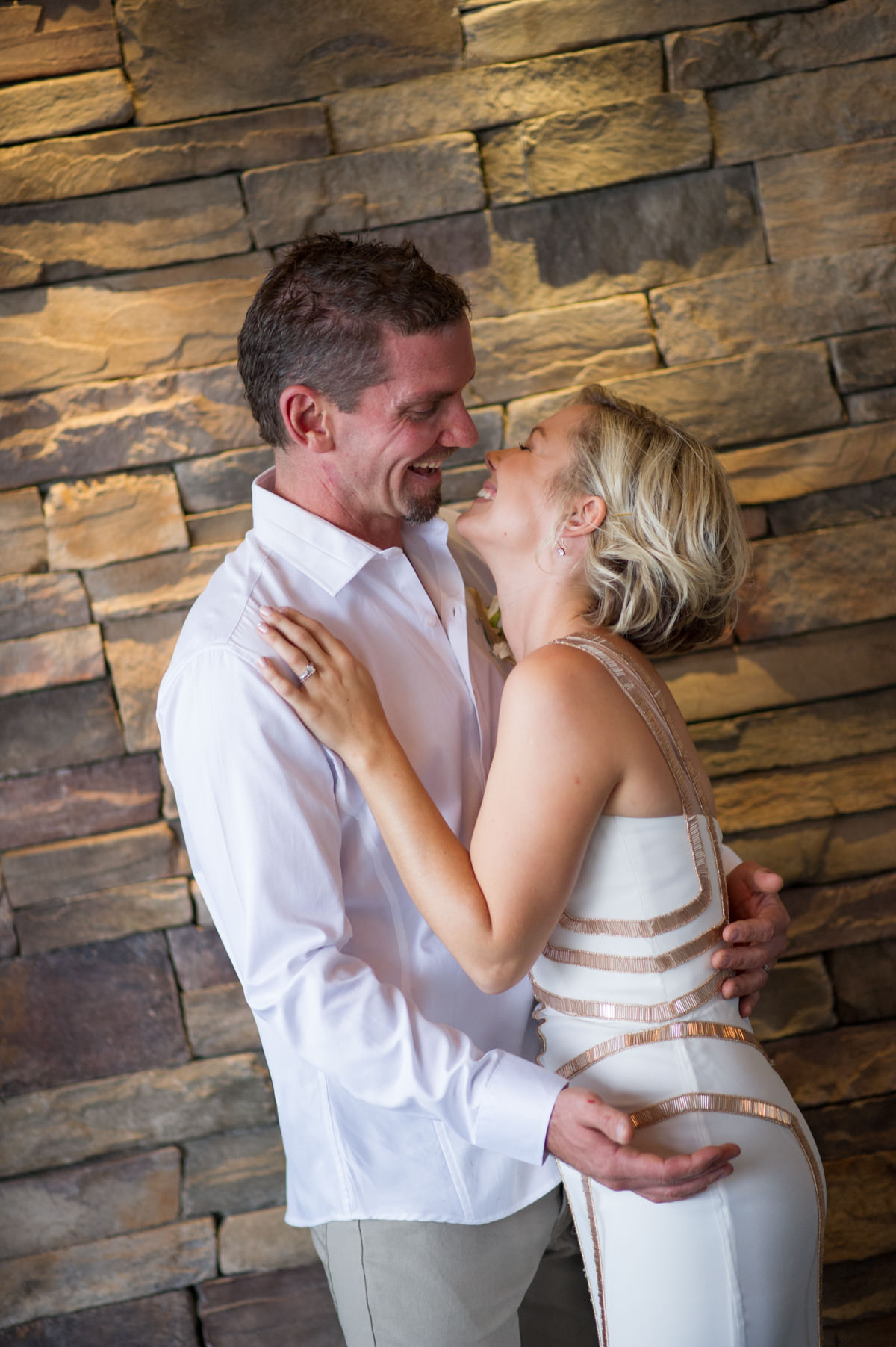 Bride and groom standing against brick wall at The Breakwater looking at each other