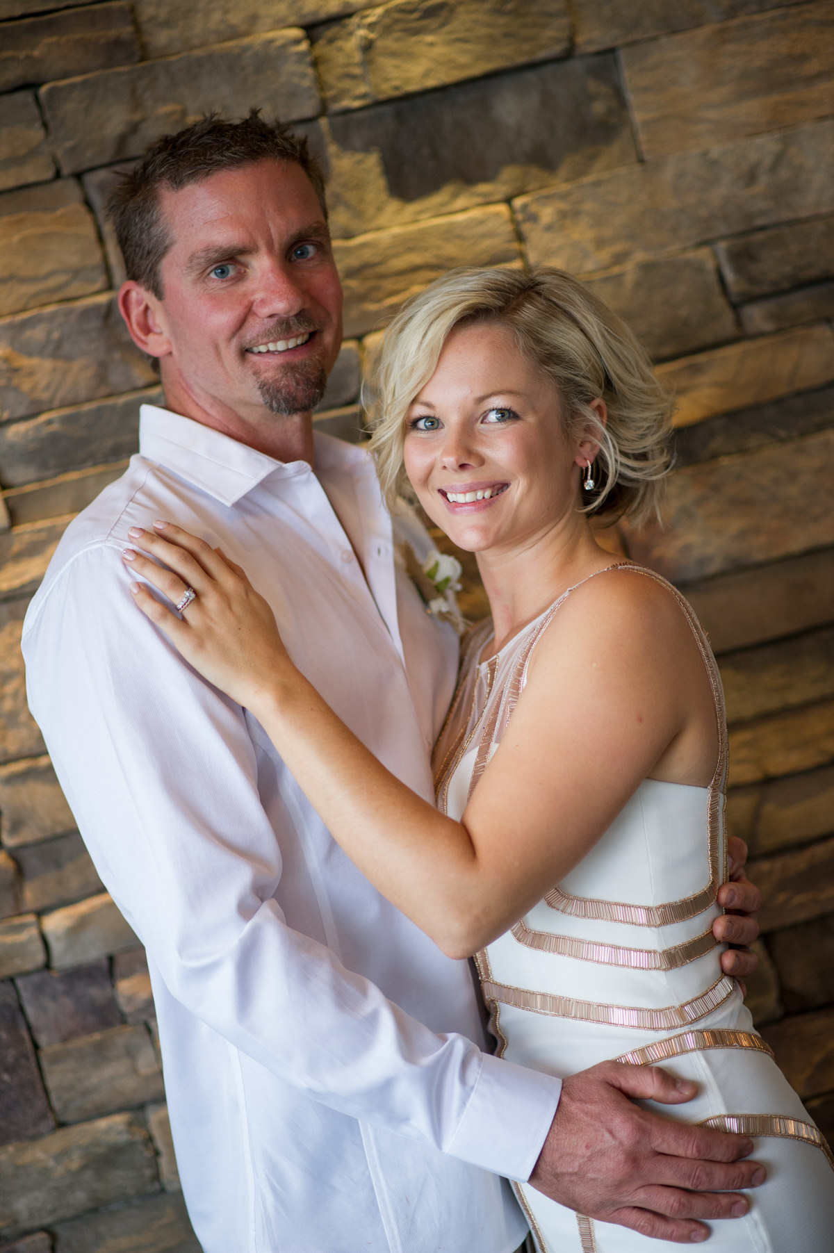 Bride and groom standing against brick wall at The Breakwater